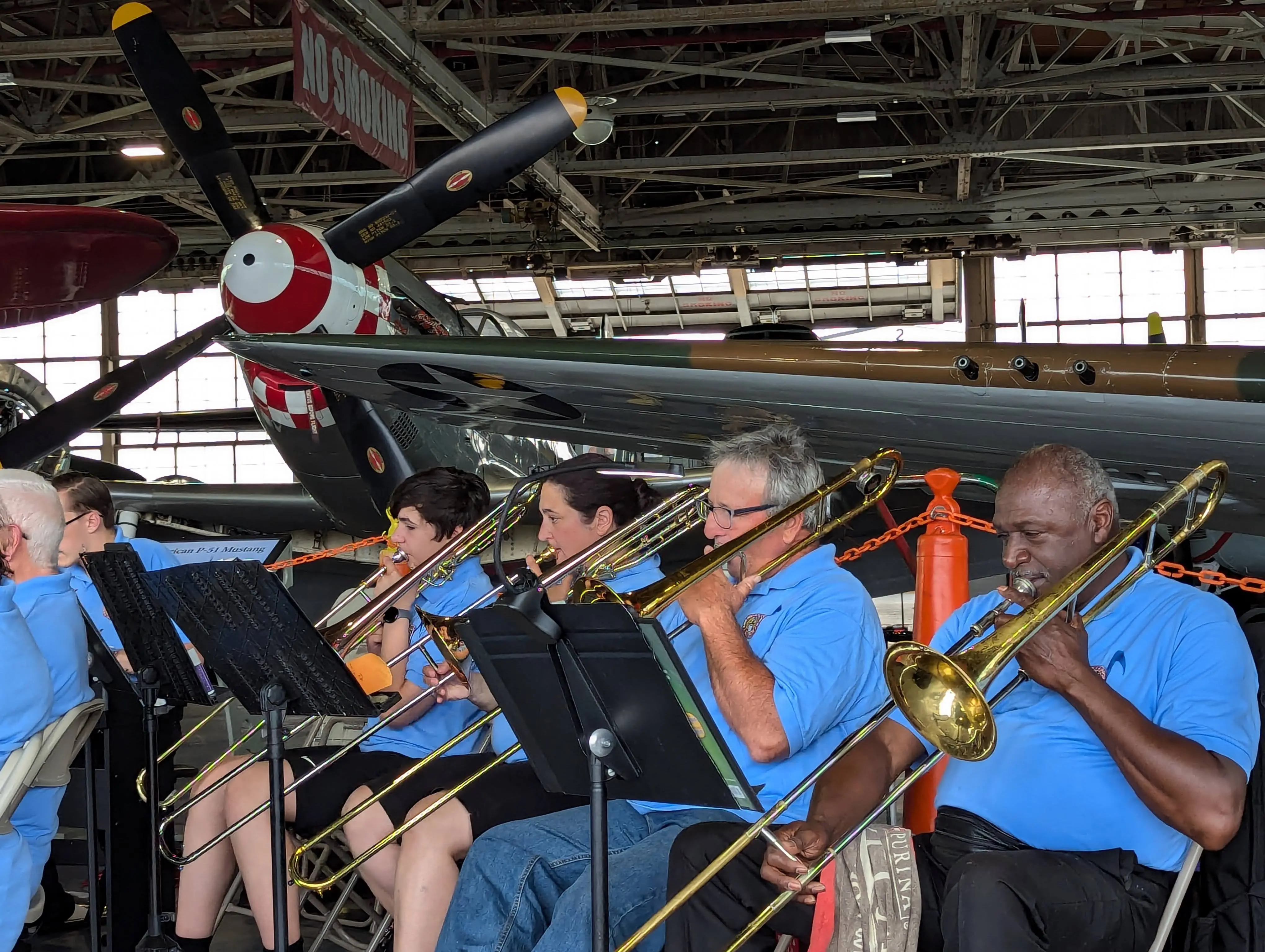Galileo Solis playing trombone in the American Airpower Museum Jazz Band beneath a P-51 Mustang fighter plane