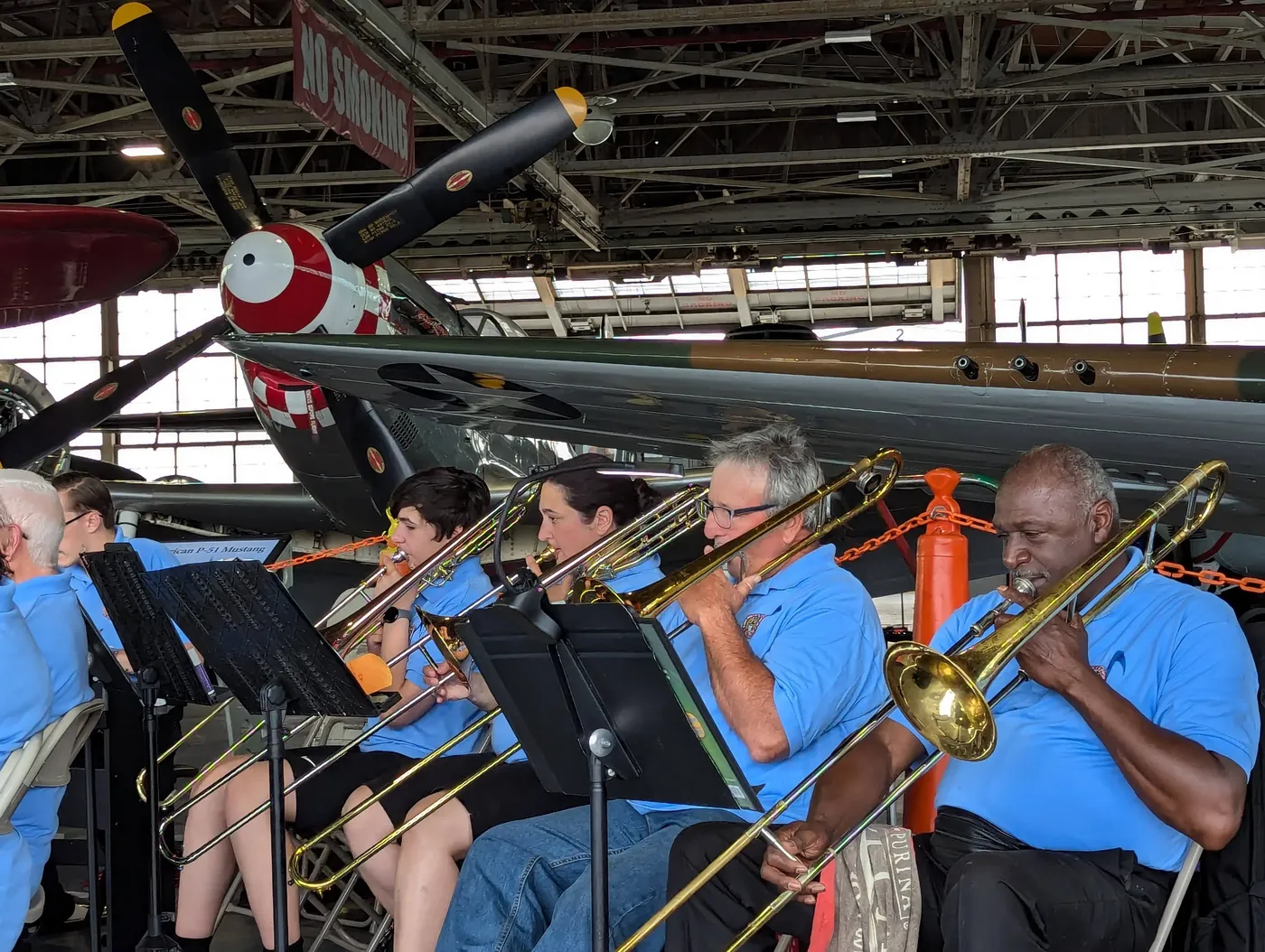 Galileo Solis playing trombone in the American Airpower Museum Jazz Band beneath a P-51 Mustang fighter plane
