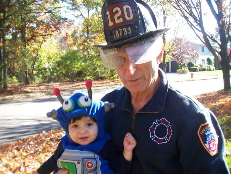 Galileo as a baby in a blue Halloween robot costume, held by Gramps in an FDNY helmet and jacket